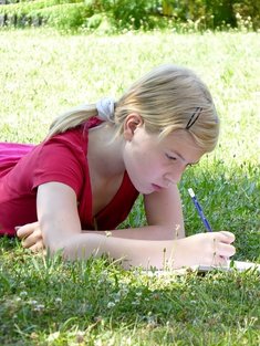 Decorative image: A middle school-aged girl is lying on a grassy area writing on an unseen book with a pencil. She wears a magenta shirt and has her hair tied back in a ponytail with a white scrunchie. Her bangs are held back with a snap barrette.